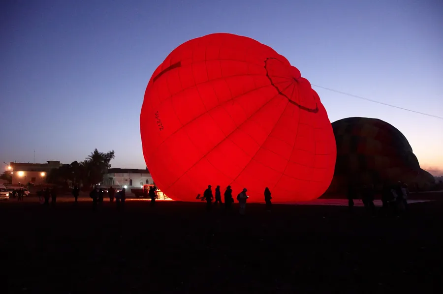 A hot air balloon glowing red as it inflates before dawn